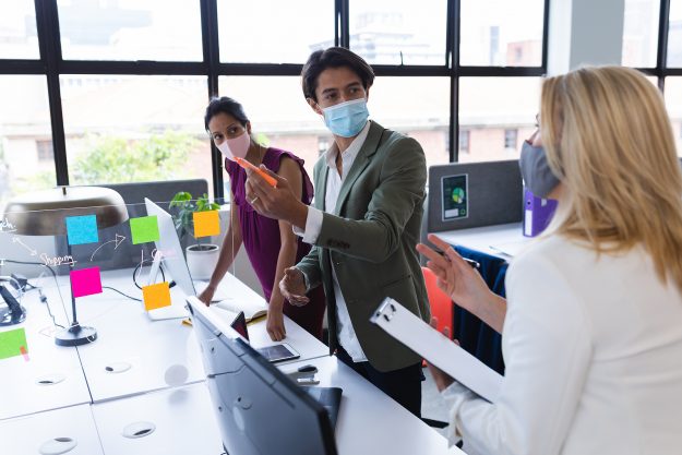 Diverse businessman and businesswomen wearing face masks discuss